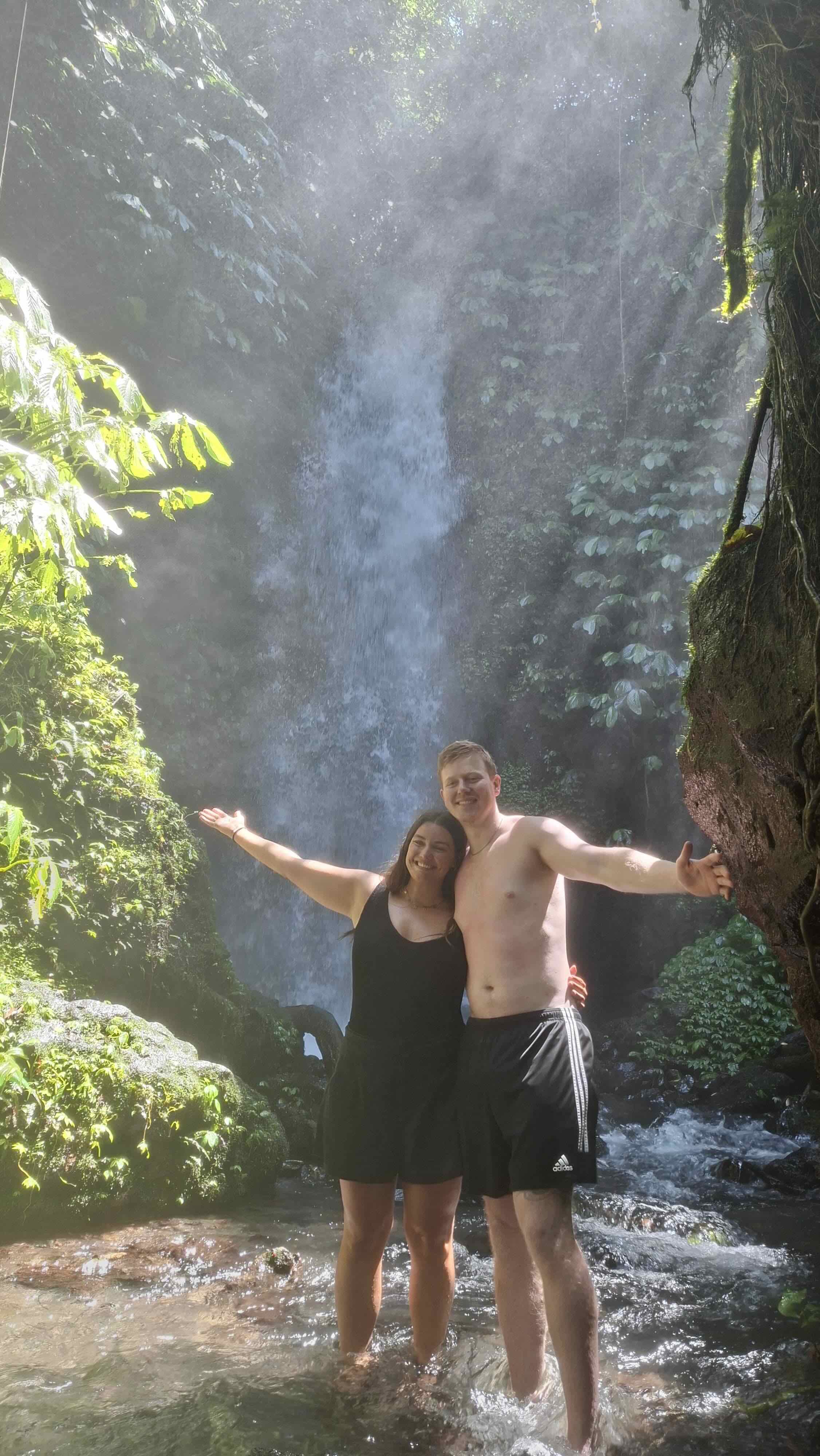 Couple embracing in front of a misty waterfall in Tetebatu